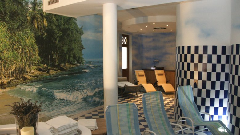 A sauna area with sun loungers, a mural of a beach and blue and white checkered tiles.