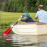 A child and an adult are rowing in a small boat on a pond.