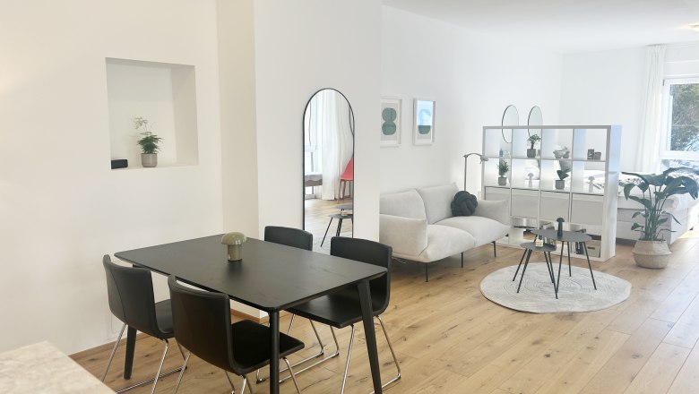Modern living room with dining table, sofa and shelves in an open space.