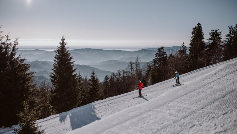 Two skiers on a slope in the Unterberg ski area with a mountain panorama in the background.