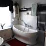 Modern bathroom with free-standing bathtub, white tiling, black towel rail and red carpet.