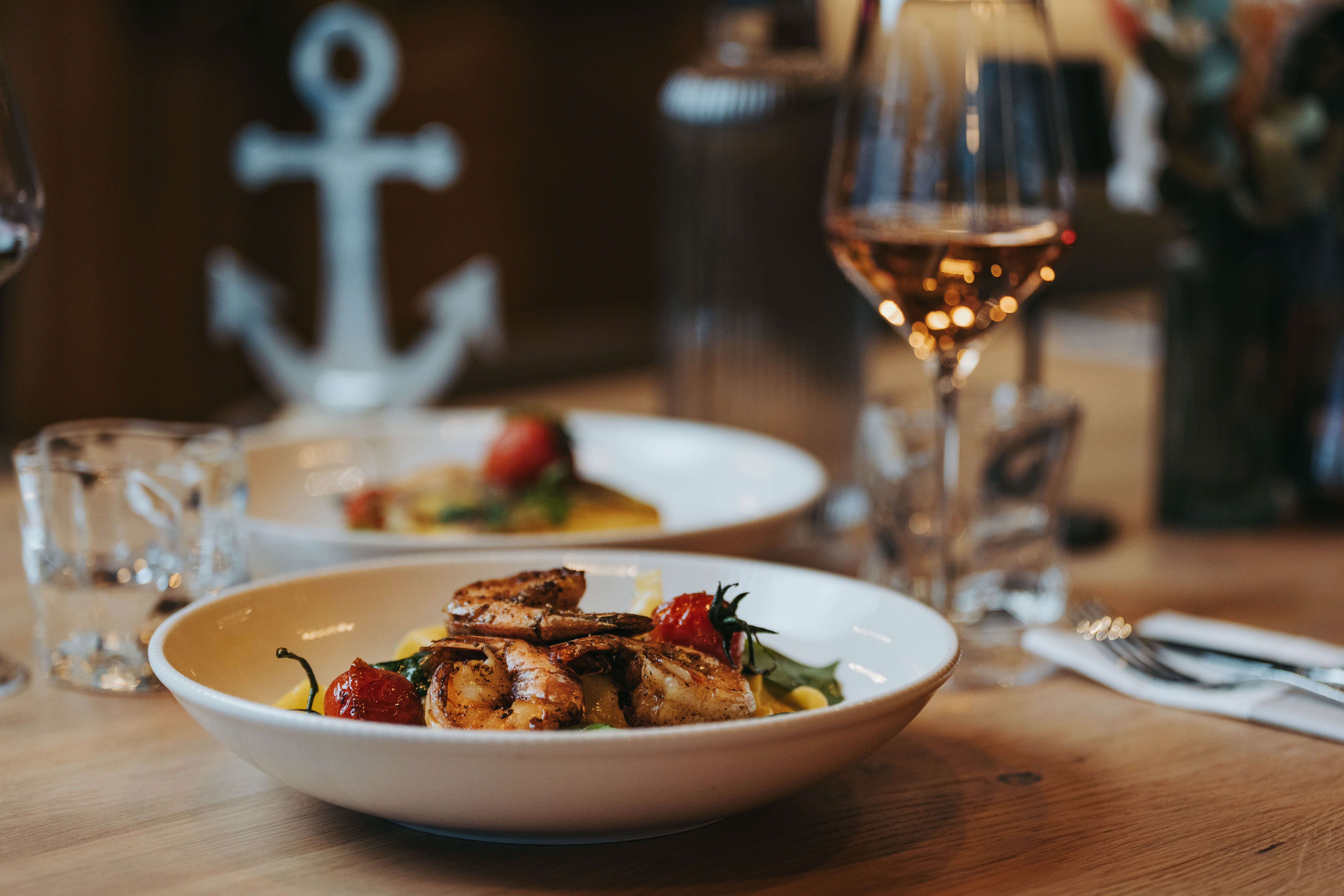 A plate of prawns and vegetables on a table, with a glass of wine next to it.