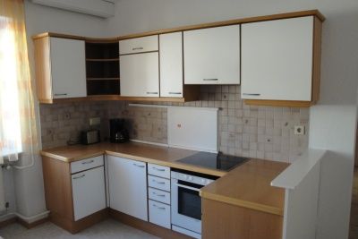 Small kitchen with white cupboards, stove and coffee machine.