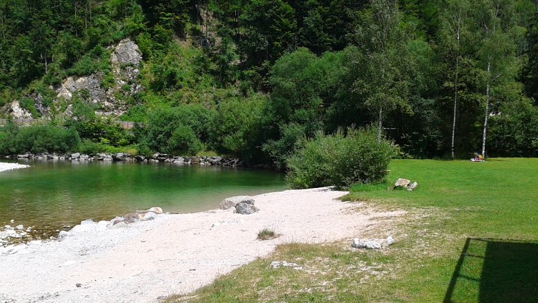 A river with clear water, surrounded by green trees and a small gravel area on the bank.