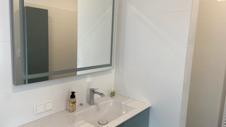 Modern bathroom with mirror, washbasin and soap dispenser.