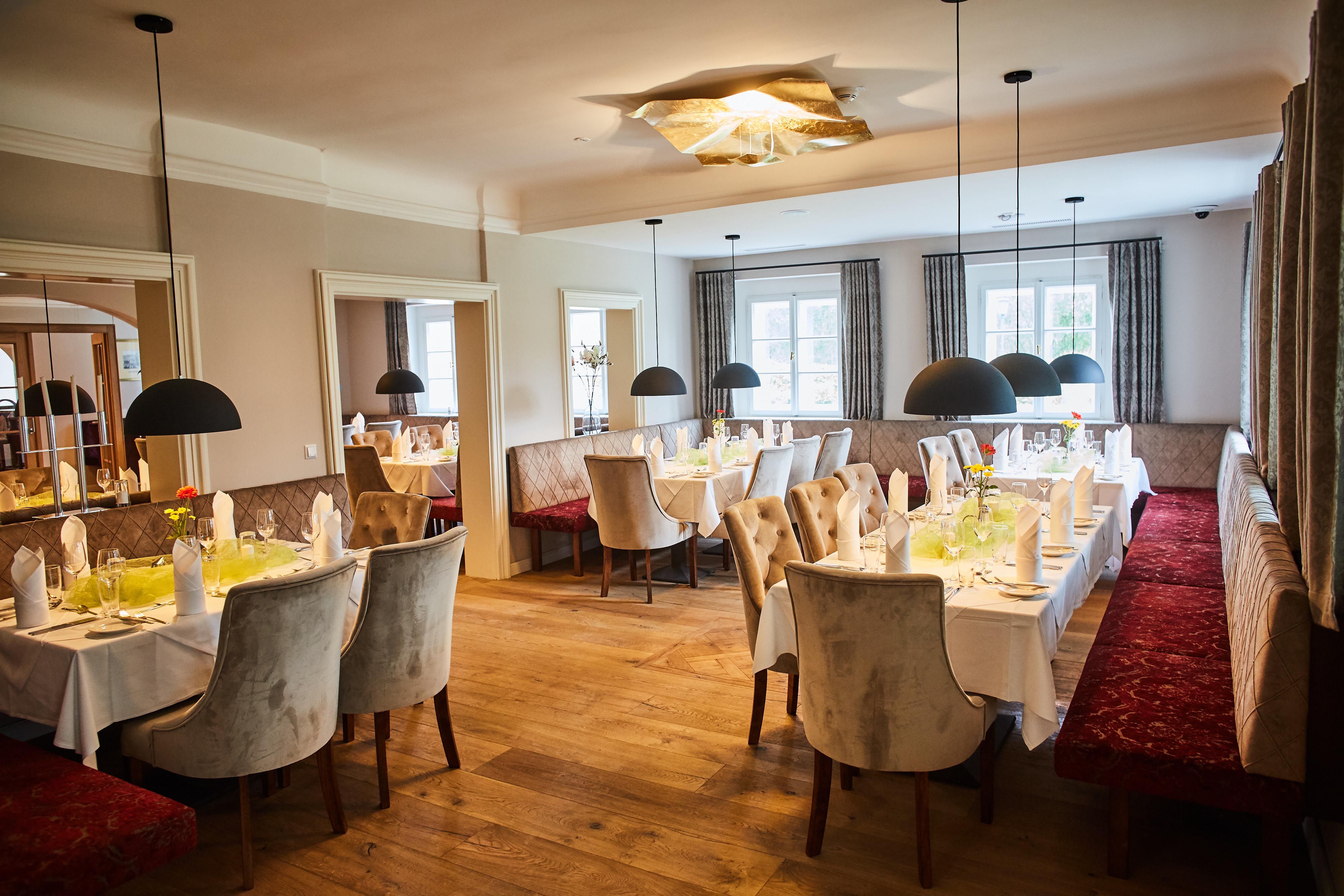 Elegant restaurant with set tables, upholstered benches and hanging lamps at Schloss Luberegg
