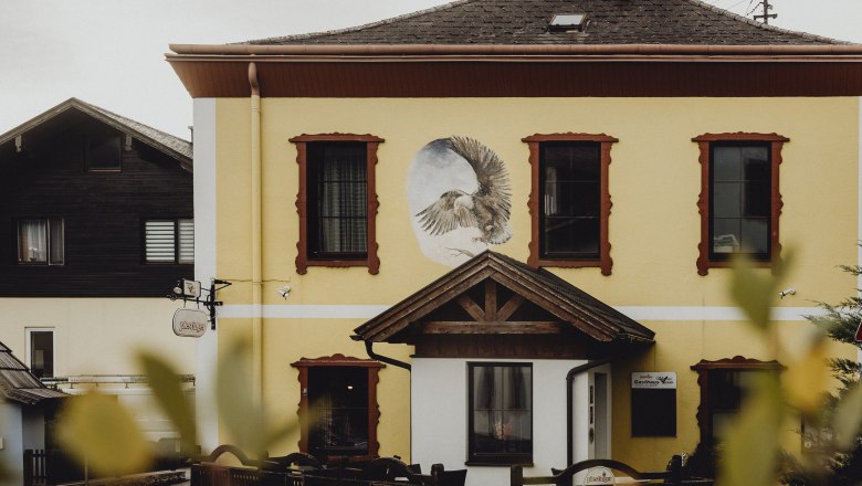 Yellow building with a mural of an eagle and red window frames.