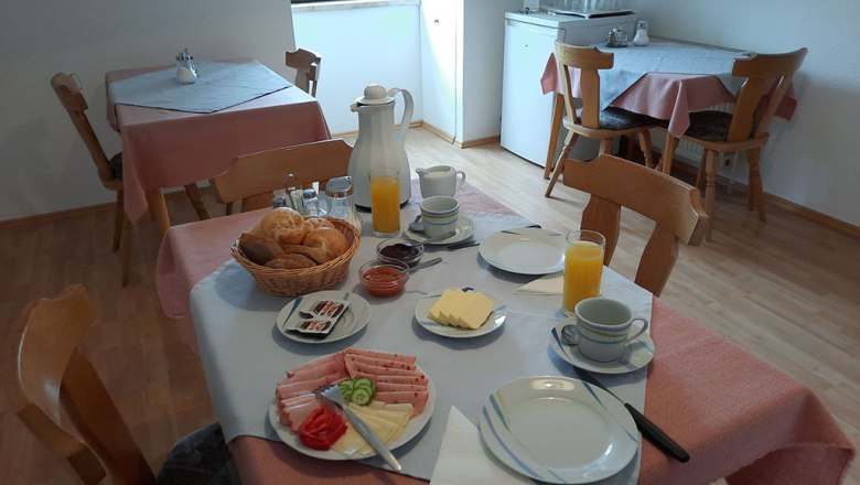 A laid breakfast table with bread rolls, cold cuts, cheese and orange juice in a cozy room.