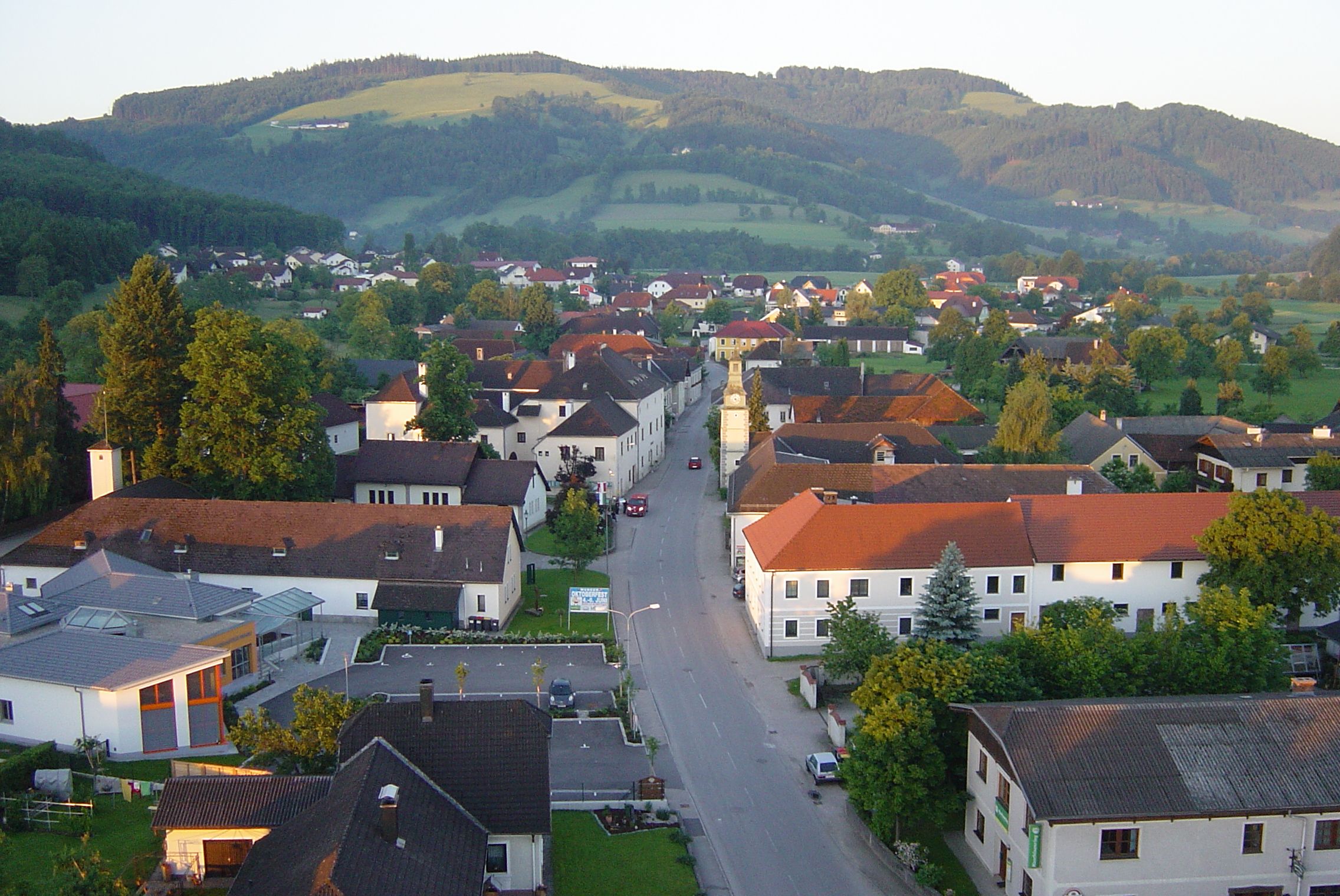 Aerial view of a village with red roofs and a green landscape in the background.