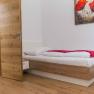 A simply furnished room with a single bed, wooden floor and a picture of red flowers on the wall.