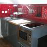 Modern kitchen with red splashback, sink, stove and microwave.