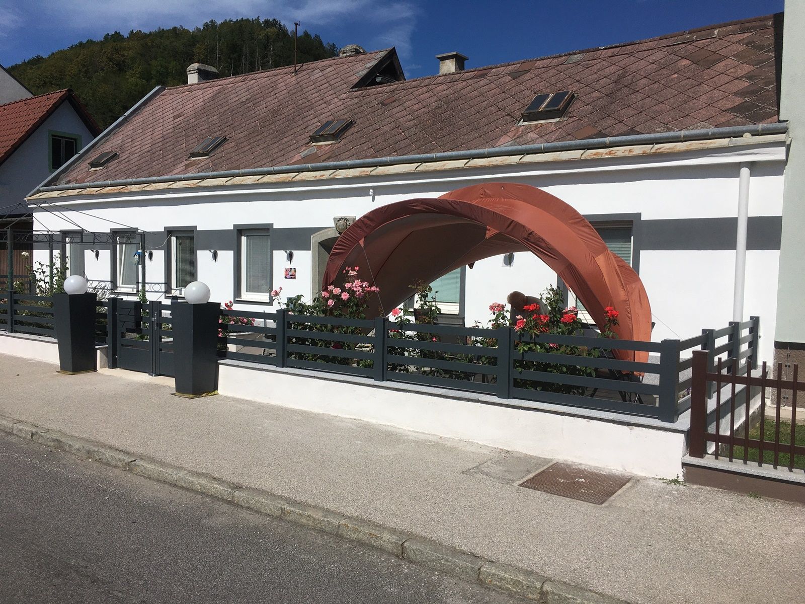 A white house with a small garden and an orange pavilion in front of the door.