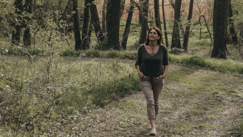 Woman walking along a forest path, surrounded by trees and greenery.