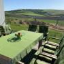 Terrace with green table and chairs, view of fields and hills.