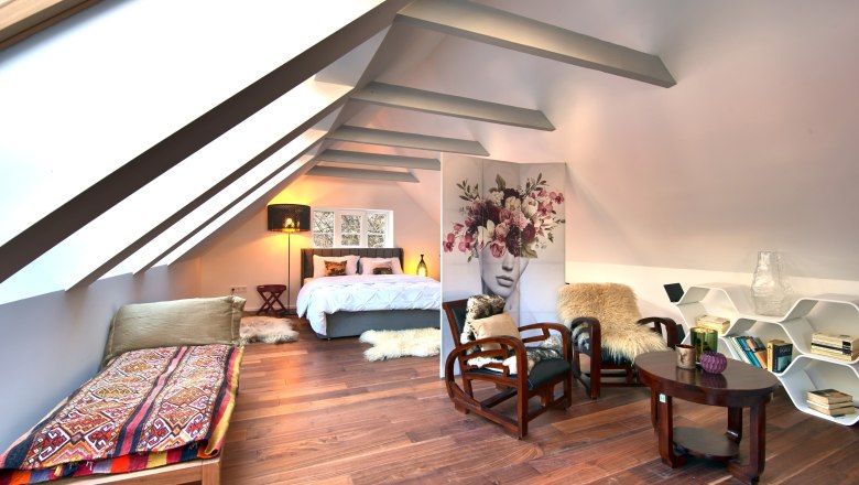 Modern bedroom in the attic with wooden floor, bed, armchairs and decorative room divider.