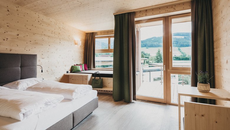Modern hotel room with wooden walls, large bed and balcony with mountain view.