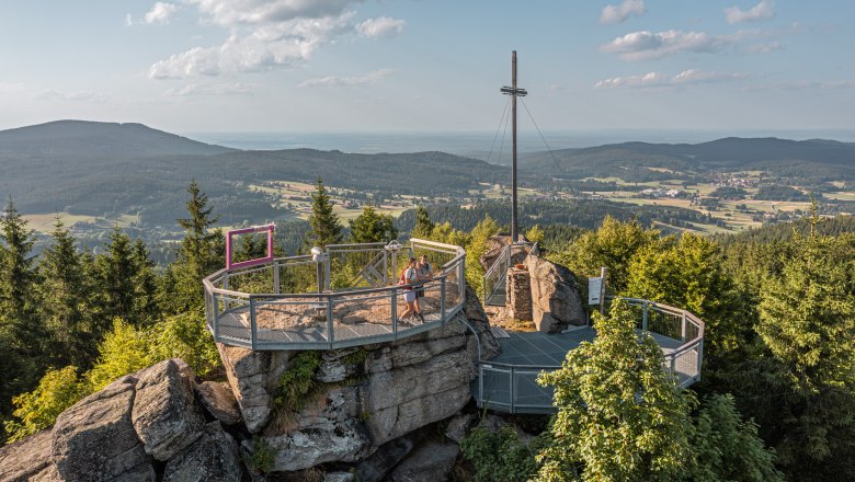 Viewing platform on a mountain with a cross and a view of the wooded landscape.
