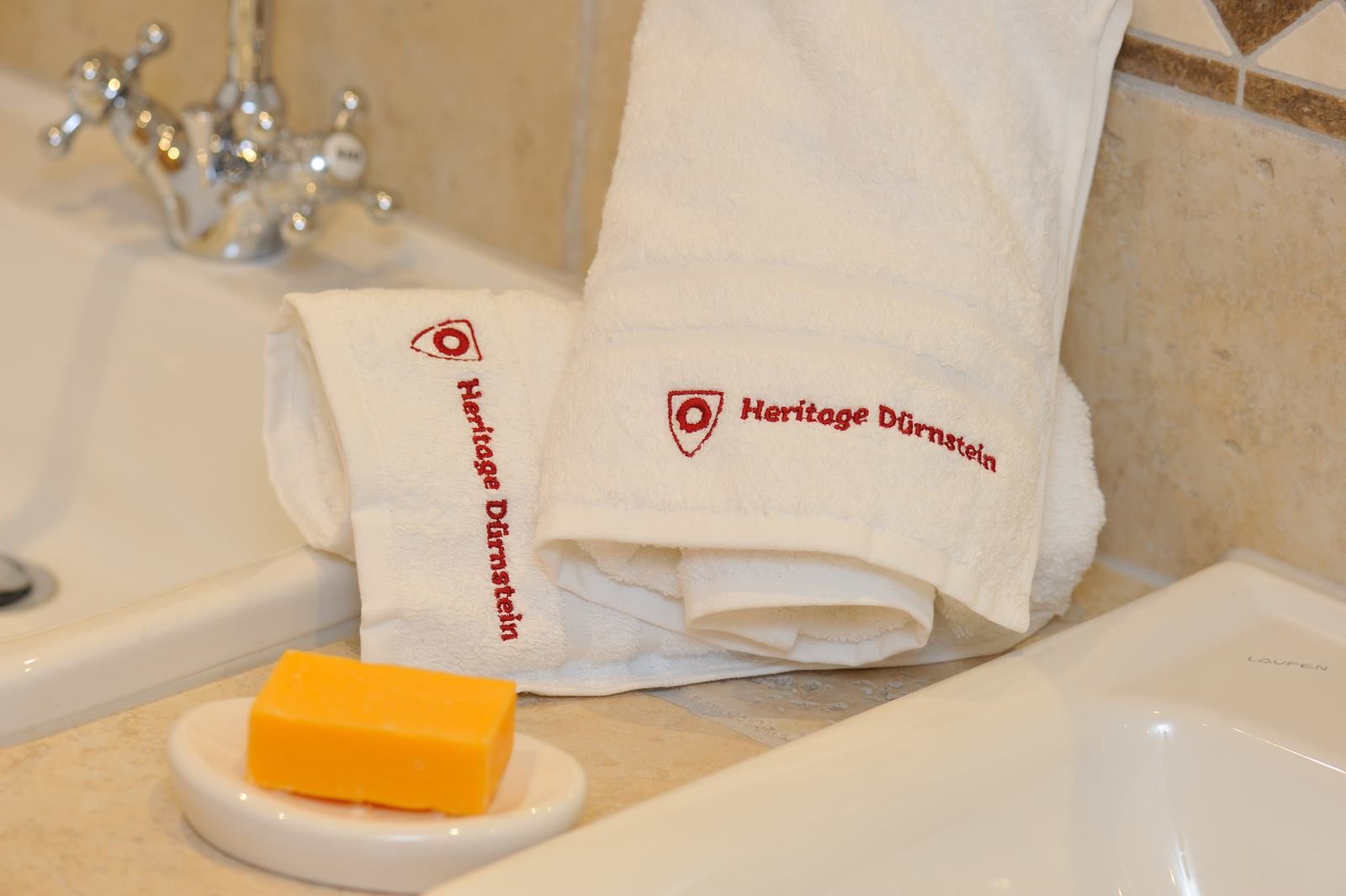 White towels with the inscription 'Heritage Dürnstein' next to a washbasin and a bar of soap.