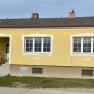 Exterior view of a yellow house with white window frames and an entrance staircase.