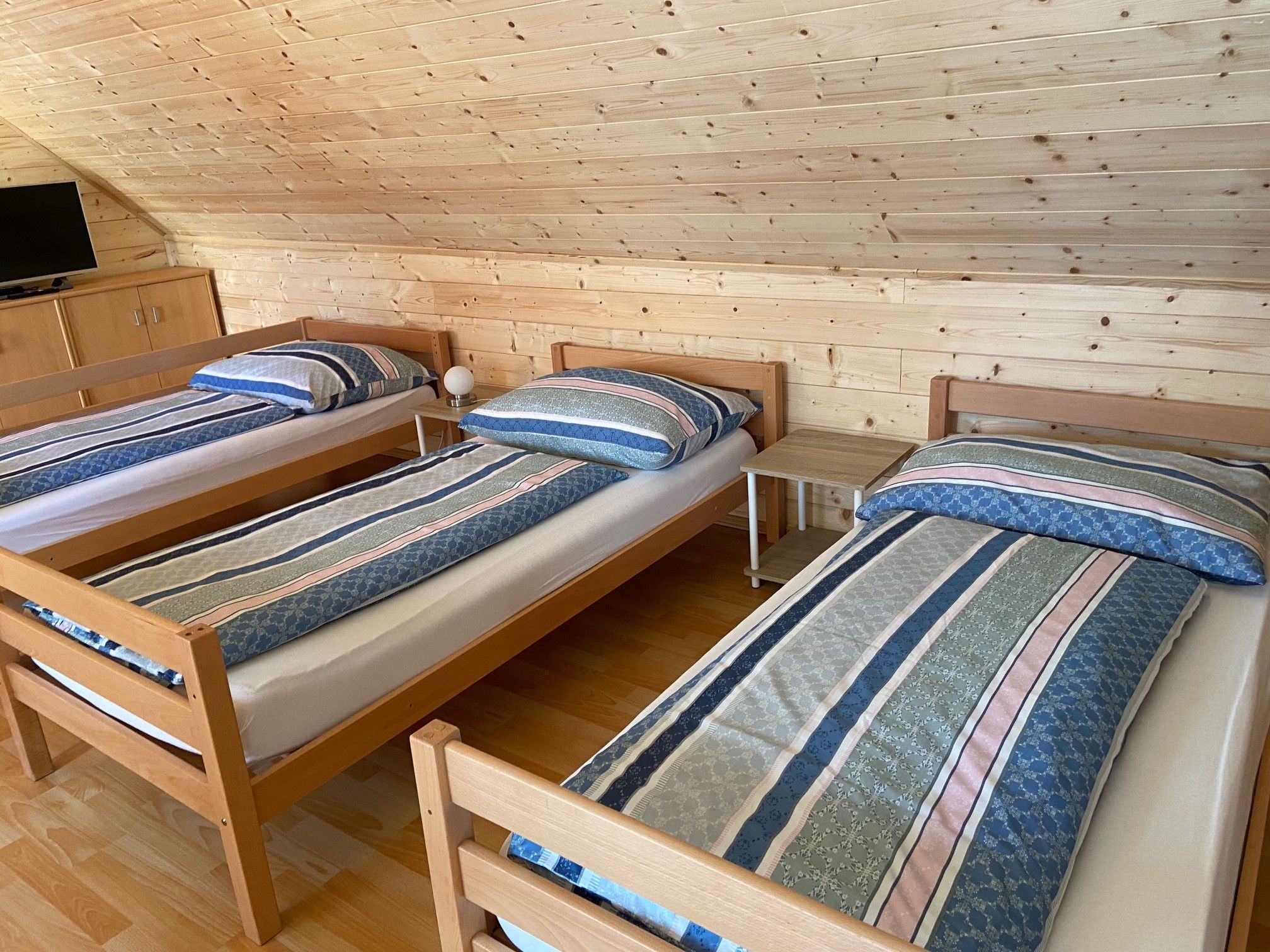 Three single beds in a room with wooden paneling and a TV.