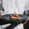 A person in a white shirt holds a plate with an elaborately prepared gourmet dish.