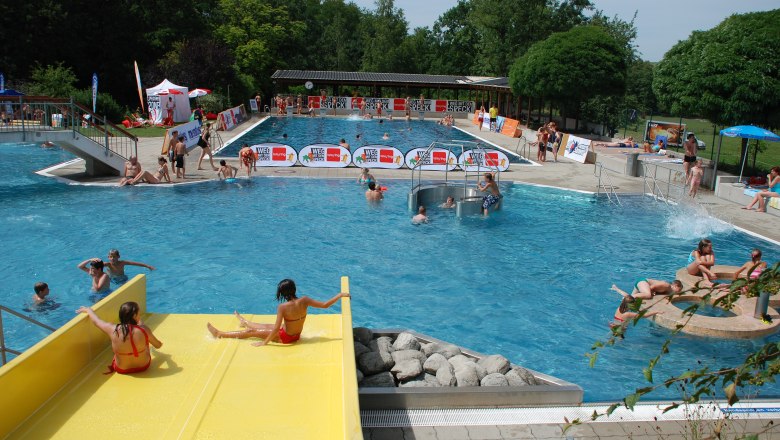 Outdoor pool with yellow slide, floats and sunbathing lawn.