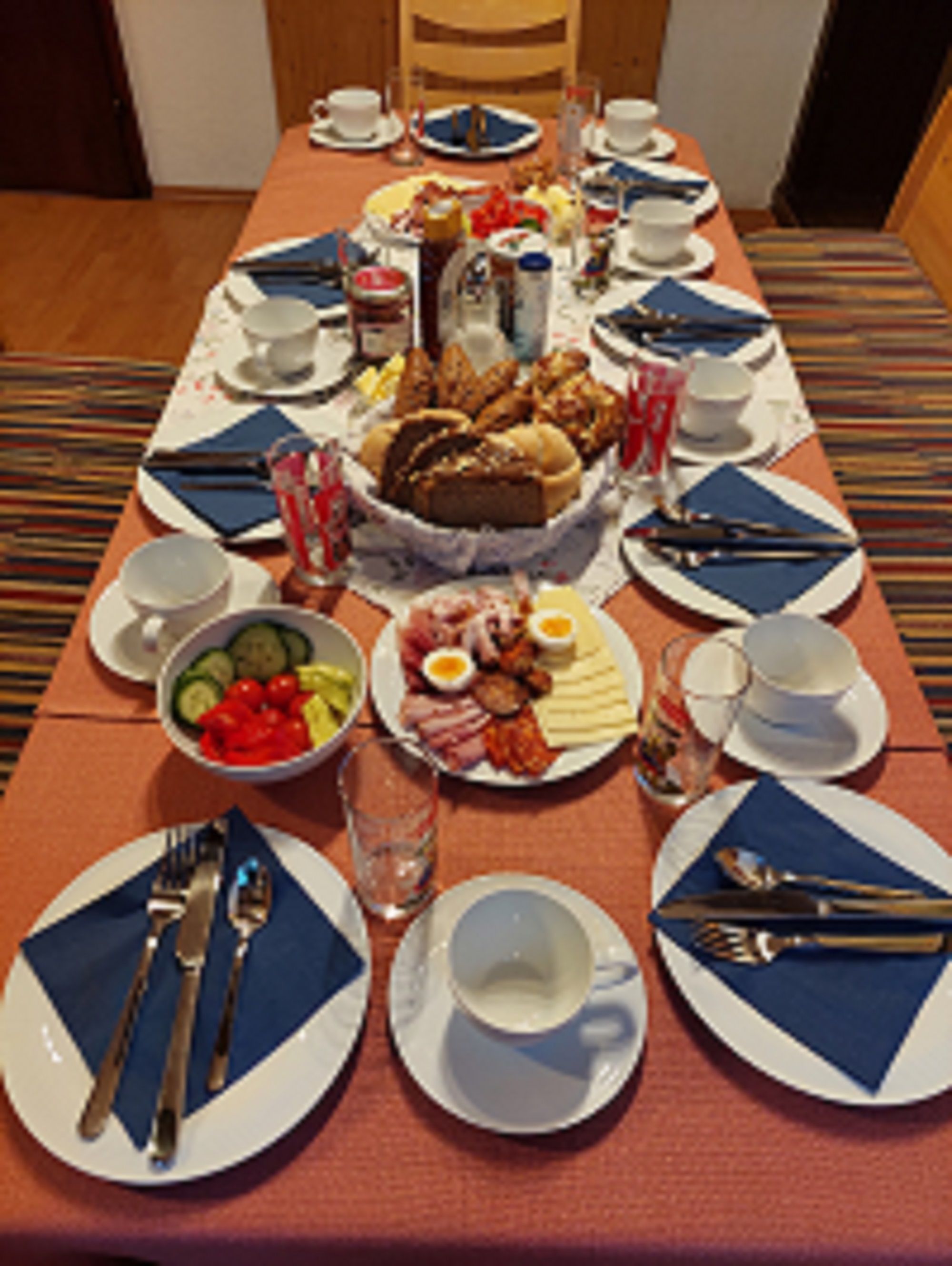 Breakfast table with crockery, bread, cold cuts and vegetables.
