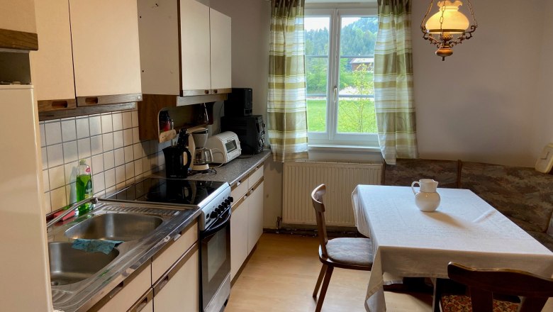Kitchen with dining table, chairs, sink, stove and window with curtains.