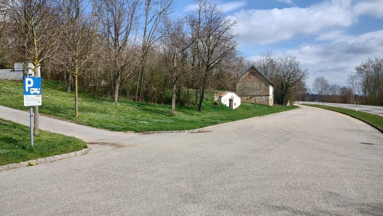 Motorhome parking space Wenzersdorf, © Gemeinde Gnadendorf Parking lot with motorhome parking sign, trees and old building in the background.