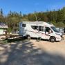 Motorhome in a parking lot in the Hohe Wand Nature Park, surrounded by trees and a blue sky.