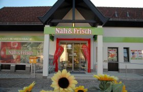 Entrance to a Nah & Frisch supermarket with sunflowers in the foreground.