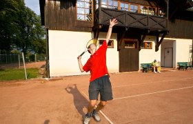 Person playing tennis in front of a building.