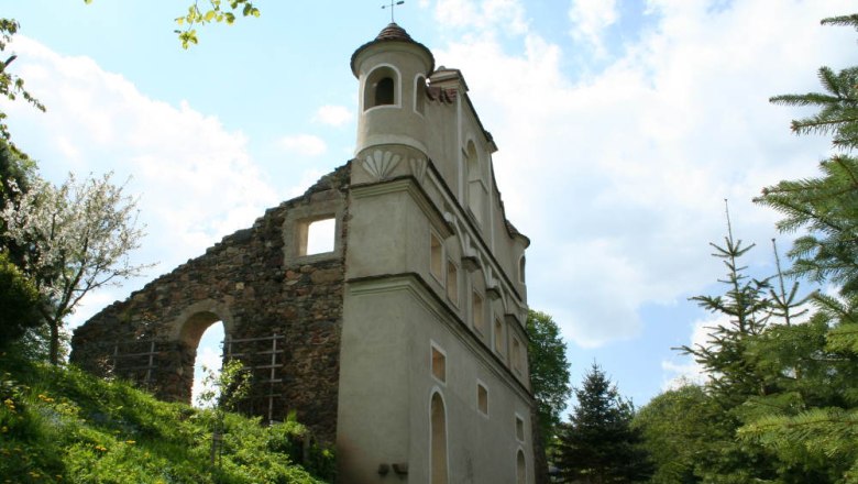Ruins of a castle with preserved tower and remains of walls, surrounded by trees and blue sky.
