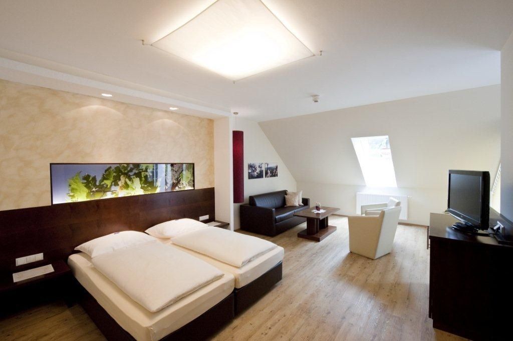 Modernly furnished hotel room with double bed, sofa, armchair and TV.