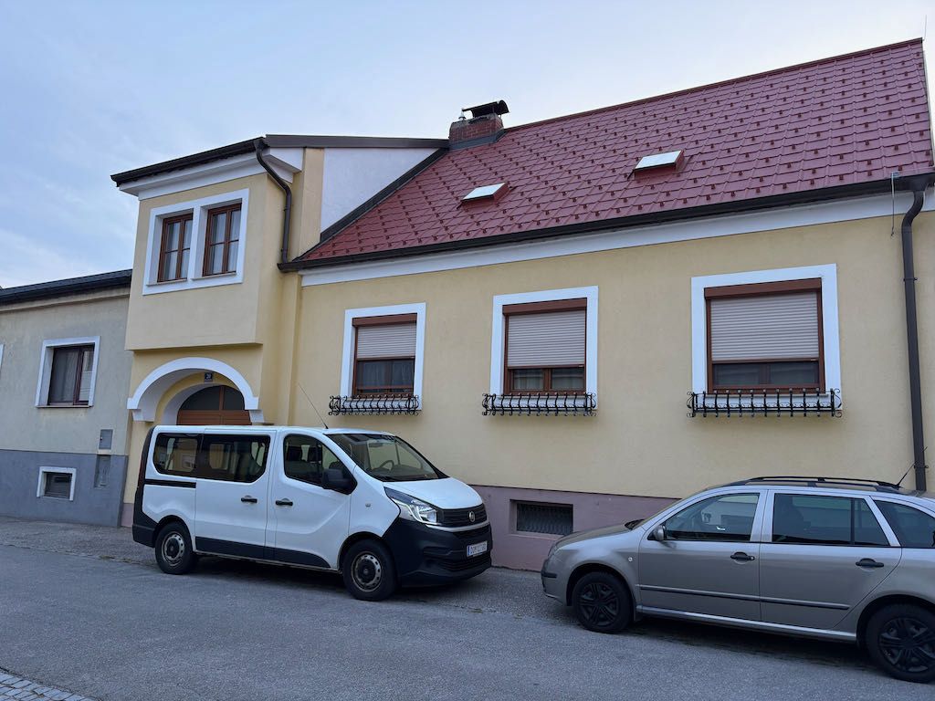 Two cars parked in front of a yellow house with a red roof.