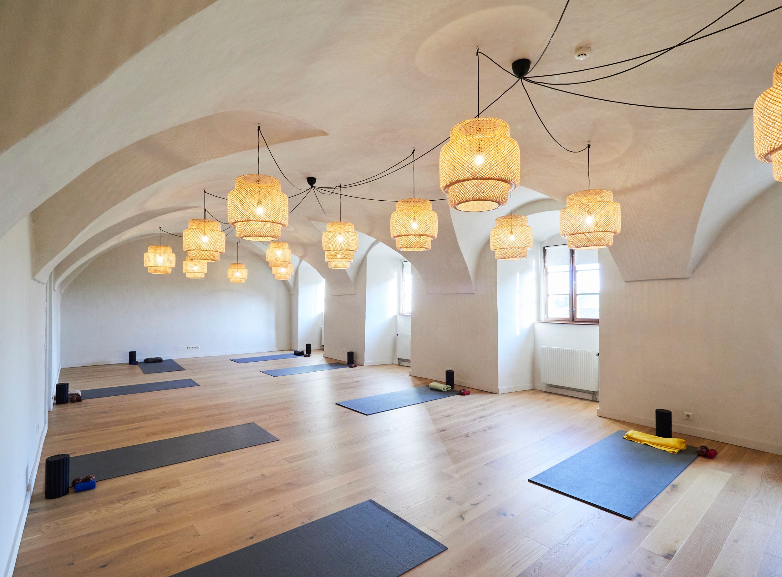 A bright yoga room with a wooden floor, mats and woven ceiling lamps in Pernegg Monastery.