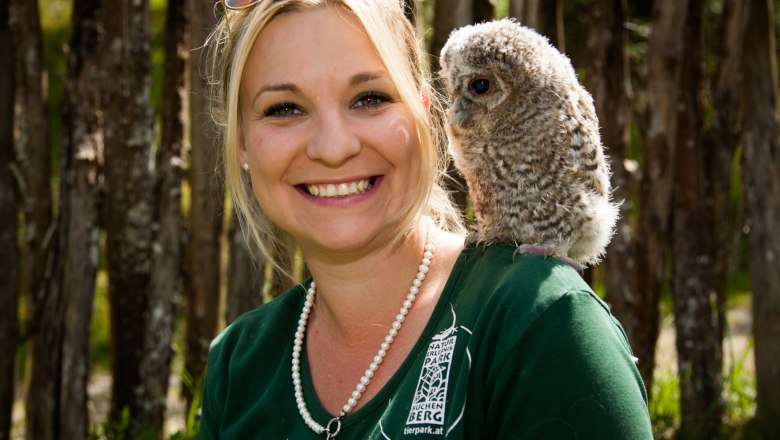 A woman laughs into the camera while an owl sits quietly on her shoulder.