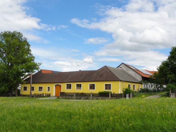 Yellow farmhouse on a green meadow with blue sky and clouds.