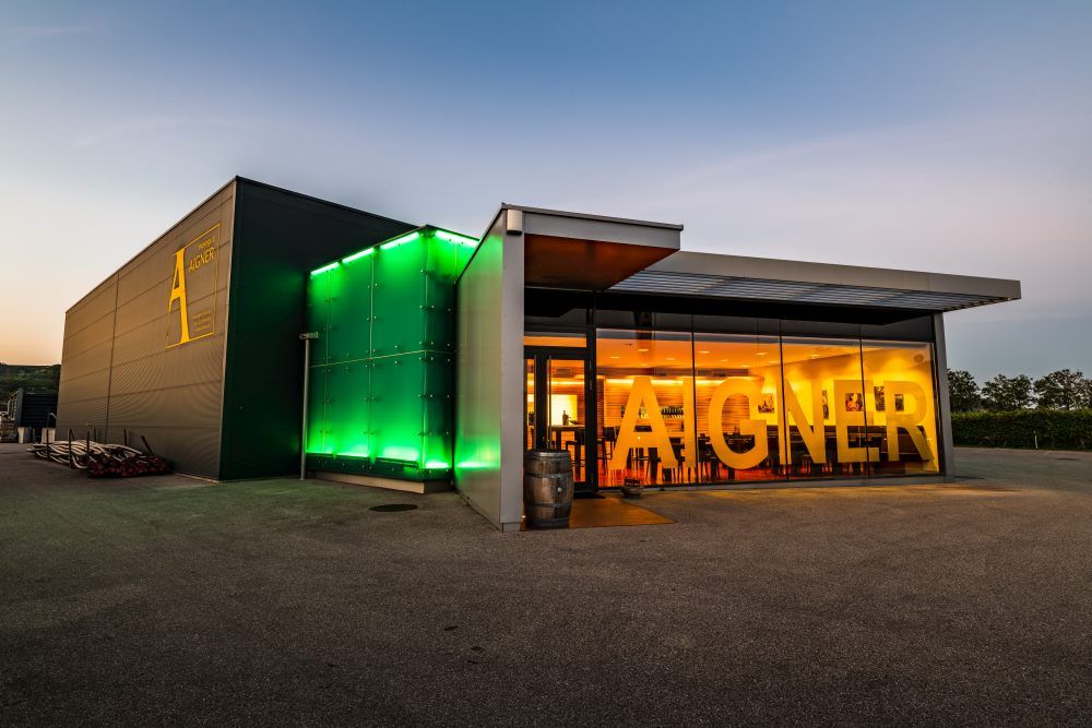 Modern winery with illuminated entrance and large 'Aigner' lettering.