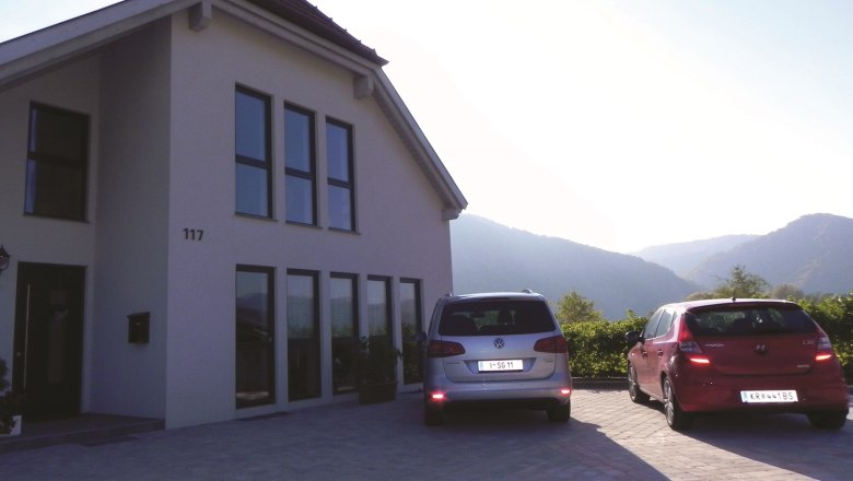 exterior_view_mensing, © Mensing Modern house facade with two parked cars on a driveway surrounded by hills.