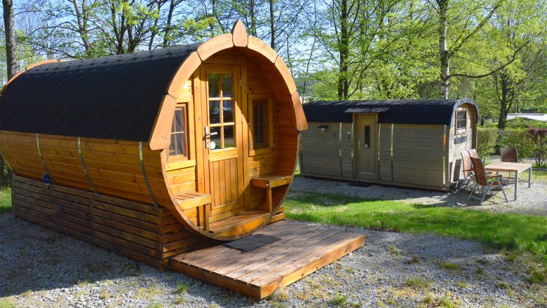 Two wooden barrel huts in a green park with trees.