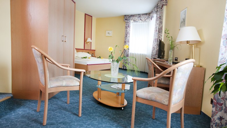 Hotel room with double bed, two chairs, glass table and TV.