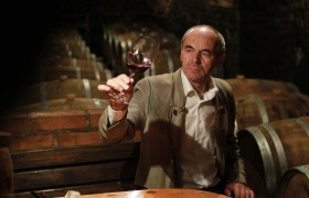 A man in the wine cellar holds up a glass of red wine.