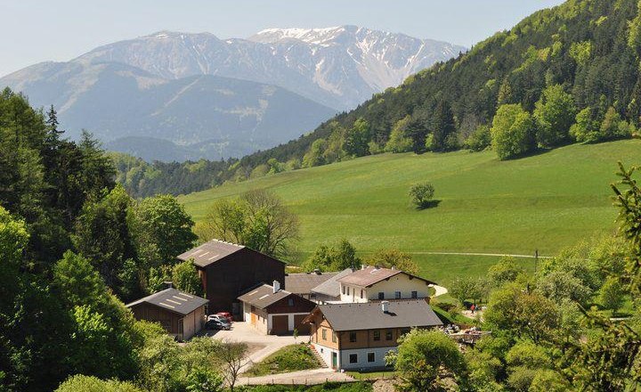 Farm in a green hilly landscape with mountains in the background.