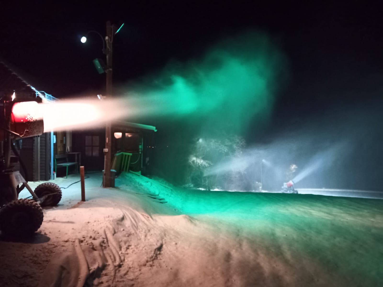 Snow cannon illuminated with green light at night.