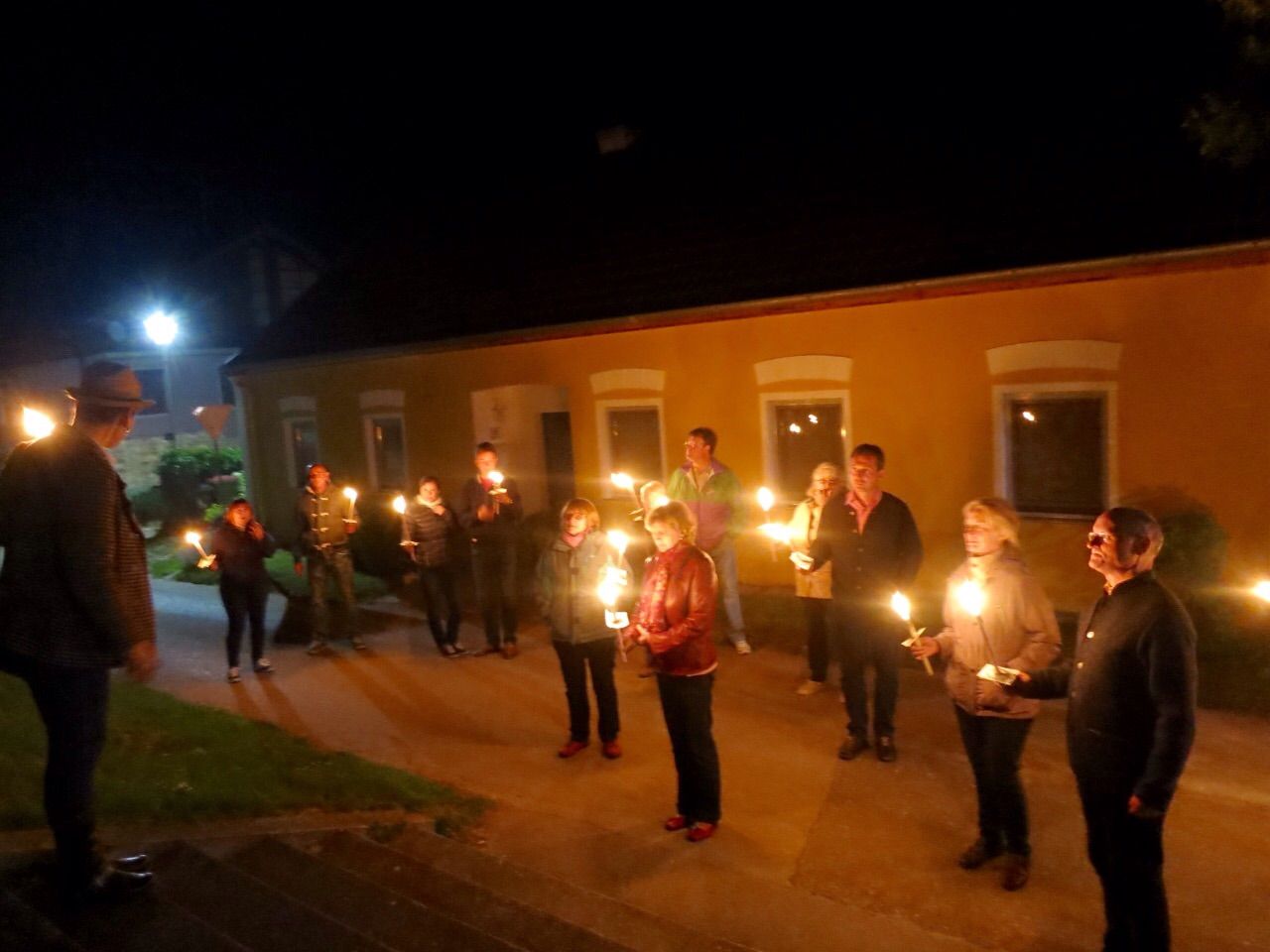People stand in front of a yellow building at night with torches.