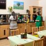 Two people help themselves to a breakfast buffet in a cozy room with wooden furniture and green tablecloths.
