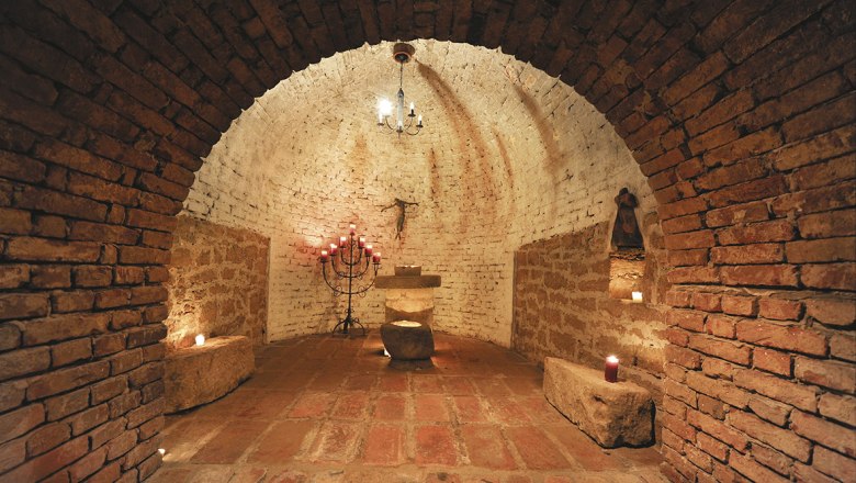 A rustic, vaulted cellar room with candles and an altar.