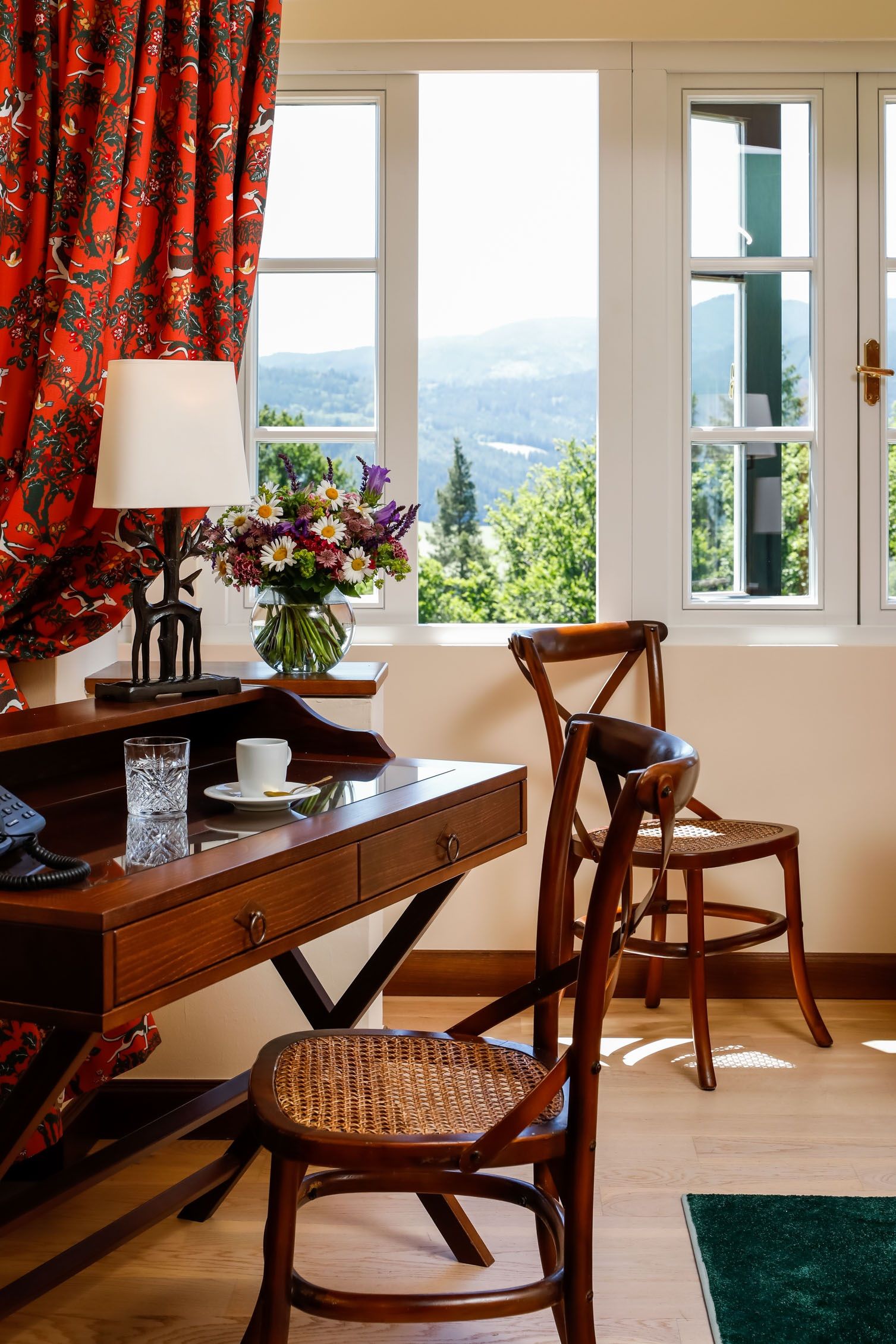 An elegant room with wooden furniture, a desk, chairs and a window overlooking a green landscape.