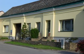 Yellow building with stone wall and plants in front of the entrance.